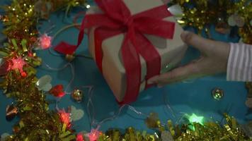 Woman's hands putting a gift box tied with red ribbon on the table is decorated with flashing light and golden material. video