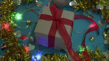 Wrapped gift box in brown paper and tied with red ribbon is setting on the table among flashing light and decorative material. video