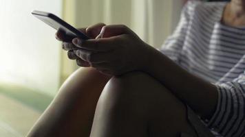 femme en tenue décontractée assise près de la porte dans sa maison SMS sur téléphone intelligent mobile pour communiquer et discuter sur les réseaux sociaux en ligne.