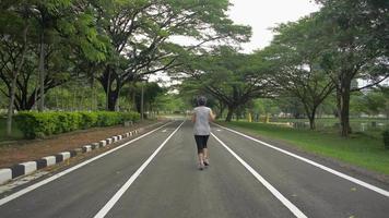 Rear view of woman in sportswear jogging on asphalt road in public park. video