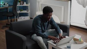 Portrait of a man in living room typing on laptop video