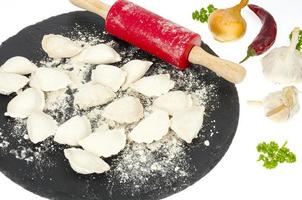 Raw cooked homemade dumplings on black plate, spices. photo