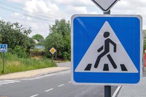 Pedestrian overground crossing, old square white with blue reflective road sign, outdoors close-up. Zebra and human sign on the background of the city. Pedestrian crossing sign. photo