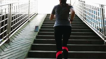 Asian woman athlete wearing earphones listening to music running on an overpass in the city sunset. video