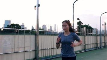 Asian woman athlete wearing earphones listening to music running on the street in the city. video