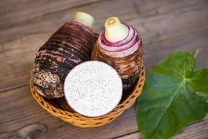 Taro root with slice half on basket and taro leaf and wooden background, Fresh raw organic taro root ready to cook photo
