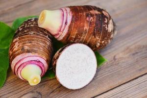 Raíz de taro con media rodaja de hoja de taro y fondo de madera, raíz de taro orgánico crudo fresco listo para cocinar foto