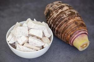 Raíz de taro con cubos de rodajas en un tazón y un fondo oscuro, raíz de taro orgánica cruda fresca lista para cocinar foto