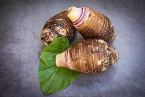 Raíz de taro sobre hojas de taro y fondo oscuro, raíz de taro orgánica cruda fresca lista para cocinar foto