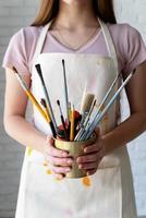 female artist hands holding a pot with paintbrushes and paints photo