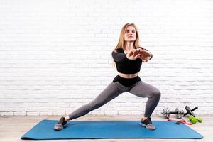 Young fit woman doing side lunges indoors on a fitness mat photo