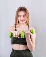 Young sportive woman doing exercises with dumbbells isolated on gray photo