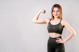 Sporty smiling woman demonstrating biceps isolated on gray background