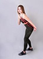 Young fit woman doing exercises with a resistance band isolated on gray photo