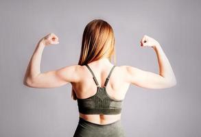 Espalda y manos de una joven mujer musculosa deportiva aislada sobre fondo gris foto