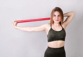 Young fit woman doing exercises with a resistance band isolated on gray photo