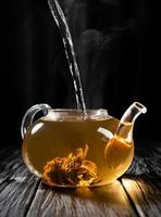 Verter agua caliente en la tetera de vidrio con té chino foto