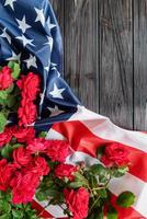 Red roses over the USA flag on dark wooden background top view flat lay