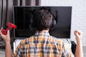 Rear view of a young man playing video games at home photo