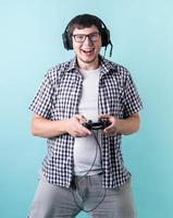 Happy laughing young man playing video games holding a joystick isolated on blue background photo