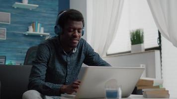 Black african american man wearing headphone, typing on laptop