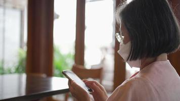 senior vrouw leest nieuws van smartphone in café