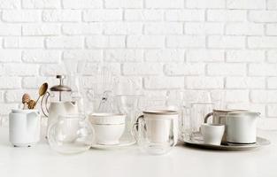 ceramic and glass cups and tableware on the table on white brick wall background photo