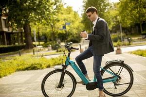 joven empresario en la bicicleta eléctrica con taza de café para llevar foto