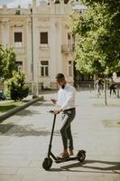 Joven afroamericano mediante teléfono móvil mientras está de pie con scooter eléctrico en una calle foto