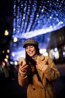 Pretty young woman using her mobile phone in the street at Christmas time photo