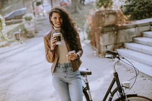 Mujer joven con teléfono móvil beber café para ir en bicicleta el día de otoño