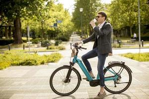 joven empresario en la bicicleta eléctrica con taza de café para llevar foto