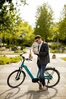 Young businessman using mobile phone by the ebike with takeaway coffee cup photo
