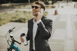 Young businessman using mobile phone by the ebike with takeaway coffee cup photo