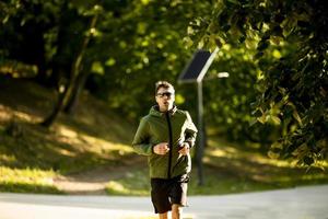 Athletic young man running while doing workout in sunny green park photo