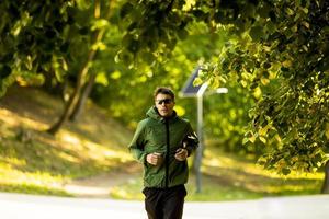 Athletic young man running while doing workout in sunny green park photo