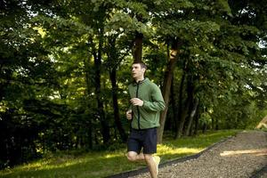 Atlético joven corriendo mientras hace ejercicio en el soleado parque verde foto