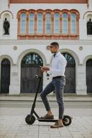 Joven afroamericano mediante teléfono móvil mientras está de pie con scooter eléctrico en una calle foto