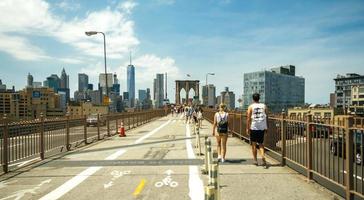 La ciudad de Nueva York, EE.UU. - 21 de junio de 2016.Los peatones caminando por el puente de Brooklyn con el horizonte de Manhattan en el fondo, en la ciudad de Nueva York