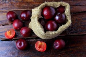 Ciruelas orgánicas crudas y frescas dentro de una bolsa de tela rústica en la mesa de madera foto