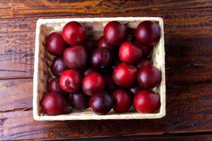 Ciruelas orgánicas crudas y frescas dentro de la caja de madera de tela rústica en la mesa rústica foto