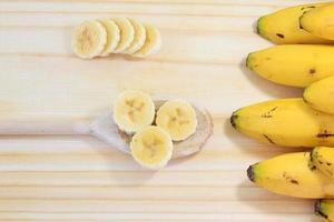 peeled banana on wood, sliced on wooden spoon, next to banana bunch photo