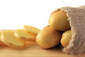 Patata que sobresale del saco en la mesa de madera, patata cortada foto