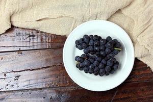 Racimos de uvas frescas, dentro de plato de cerámica, sobre mesa de madera rústica foto