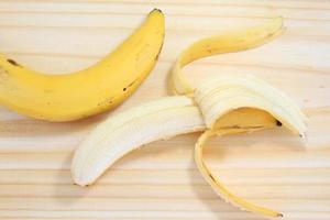 peeled banana on wood next to banana with peel photo