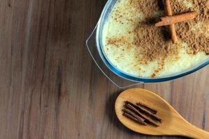 rice pudding with cinnamon in glass container on wooden table, wooden spoon beside