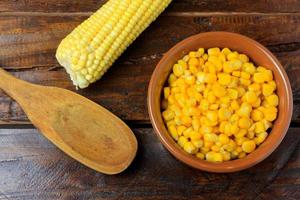 Raw corn kernels, inside ceramic bowl, next to wooden spoon on rustic wooden table. space for text photo