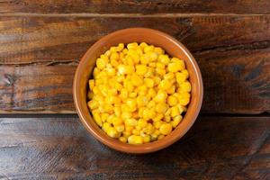 Raw corn kernels inside ceramic pot on rustic wooden table. space for text photo