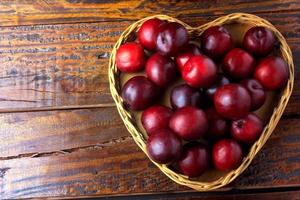 raw and fresh organic plums inside basket with heart shape on rustic wooden table. Copy space photo