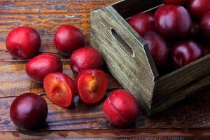 Ciruelas orgánicas crudas y frescas dentro de la caja de madera de tela rústica en la mesa rústica foto